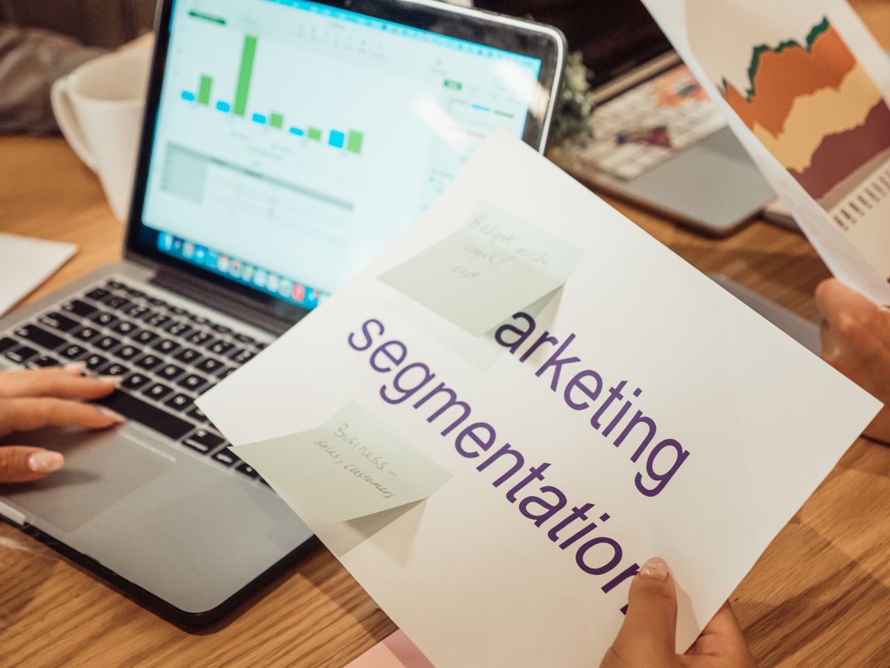 Un espace de travail moderne où l’on voit des mains analyser des données marketing sur un ordinateur portable et des documents papier.