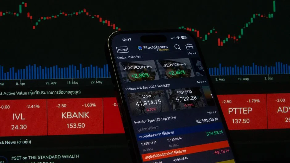 Hands using smartphone trading app with charts, dollar bills in background.